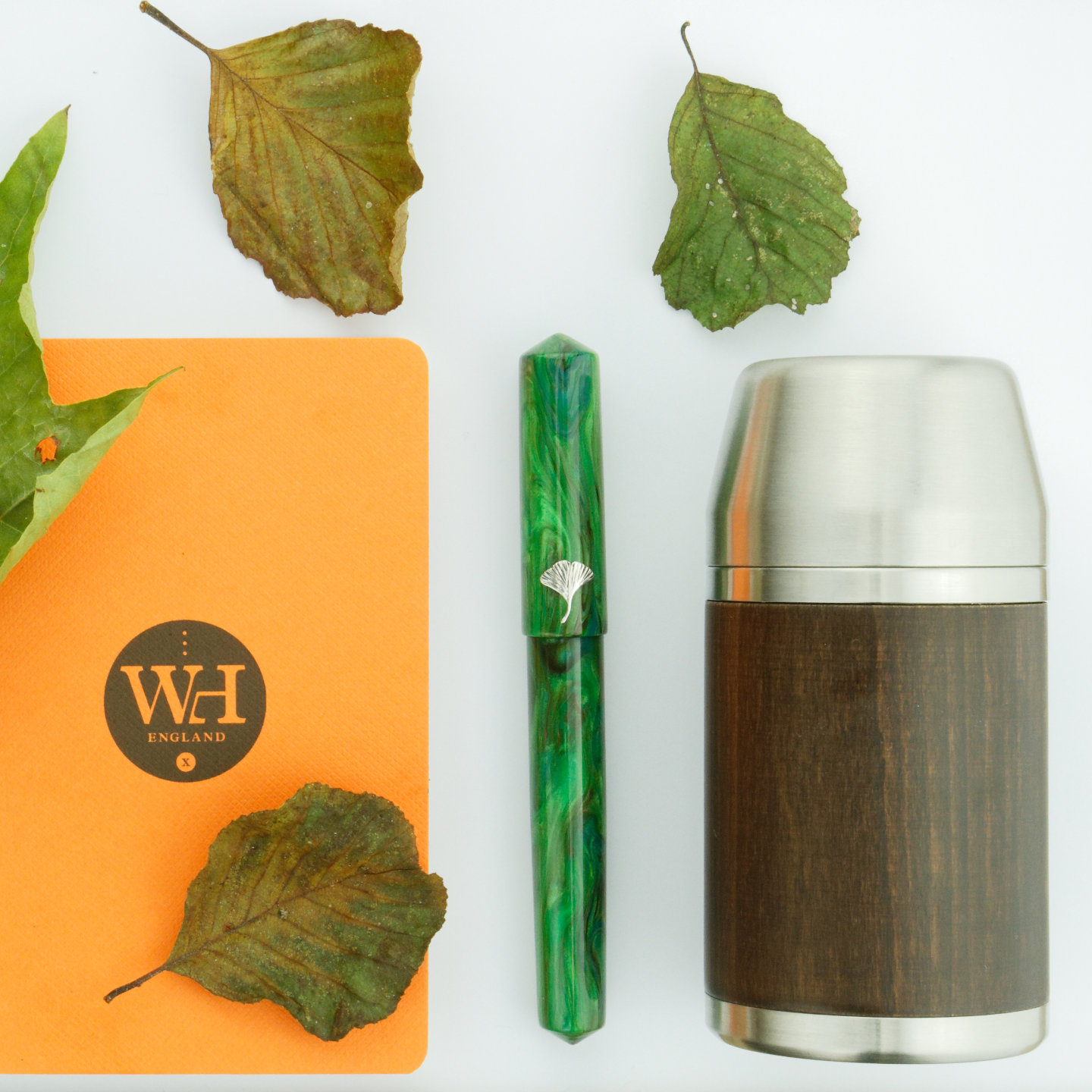 Giants' Pens Het Groene Woud fountain pen with leaves, an orange William Hannah notebook and a Nisnas Industries Upper cut flask